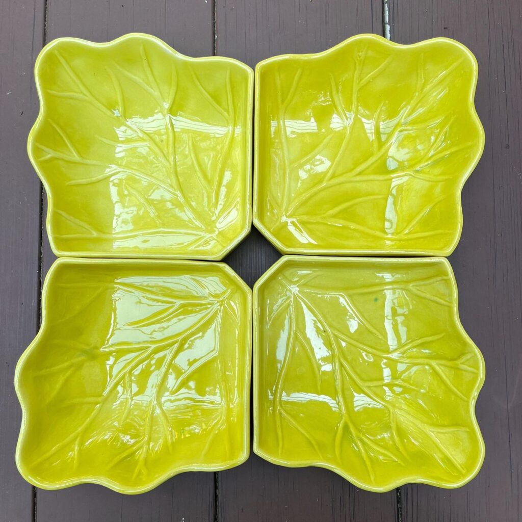 Four chartreuse green leaf-shaped ceramic plates arranged on a dark wood background, showing detailed leaf vein textures for a botanical tablescape.