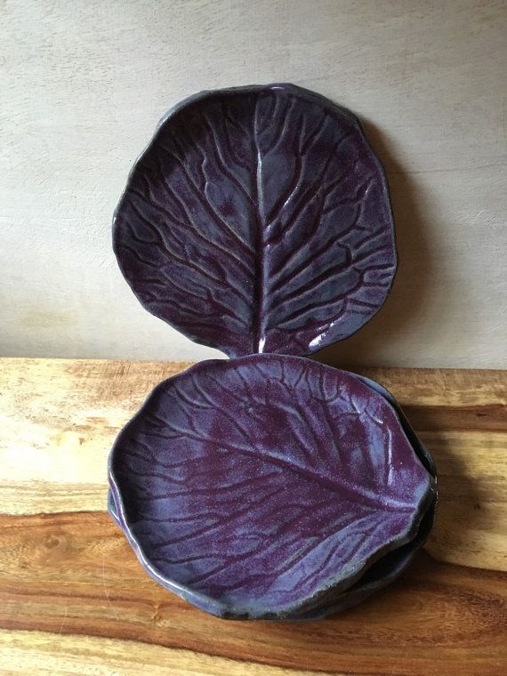 A stack of deep purple glazed ceramic radicchio cabbage plates resting on a warm wood surface against a neutral backdrop.