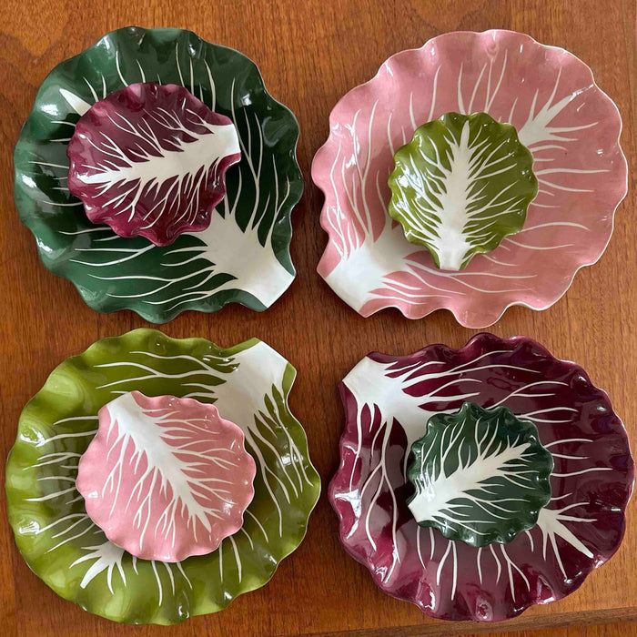 An eclectic stack of colorful nested ceramic cabbageware plates and salad bowls in green, pink, and deep plum burgundy.